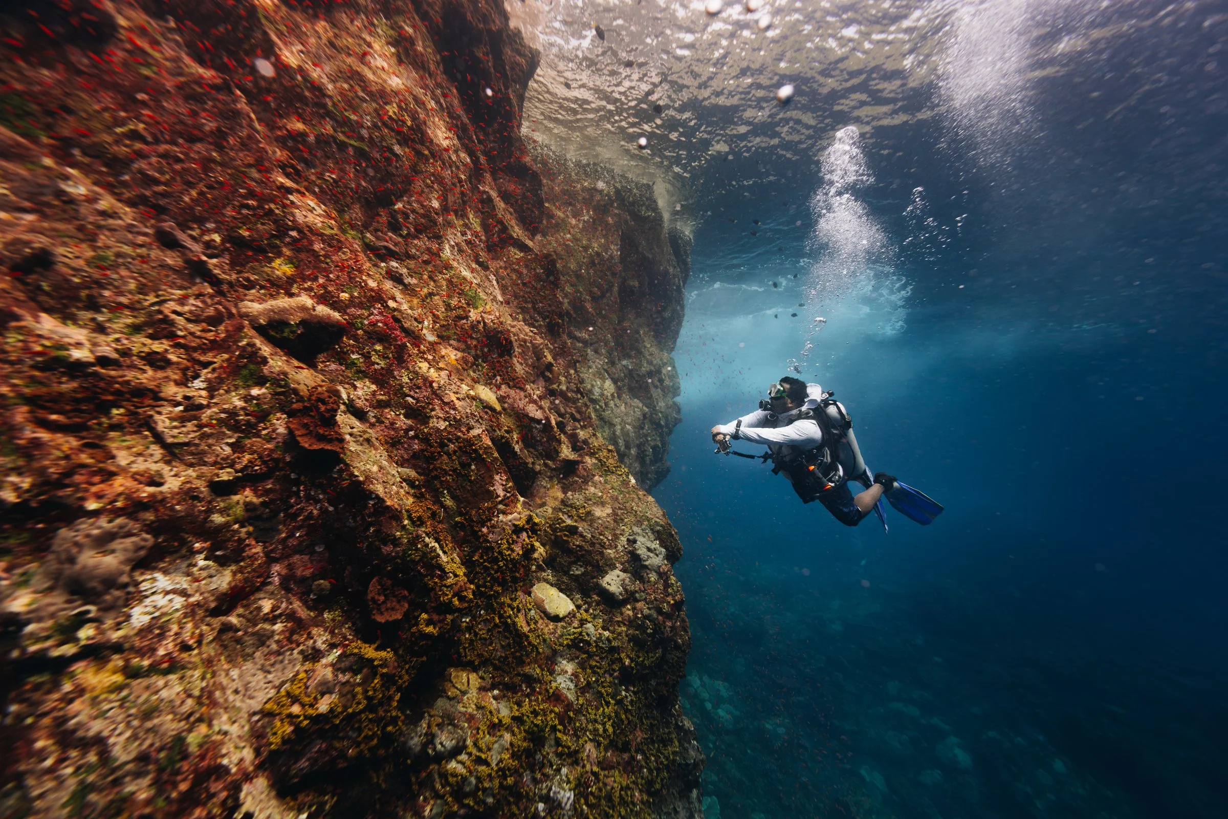 Scuba diver with tank and regulator beside a rocky underwater wall, supplied by Andamanica