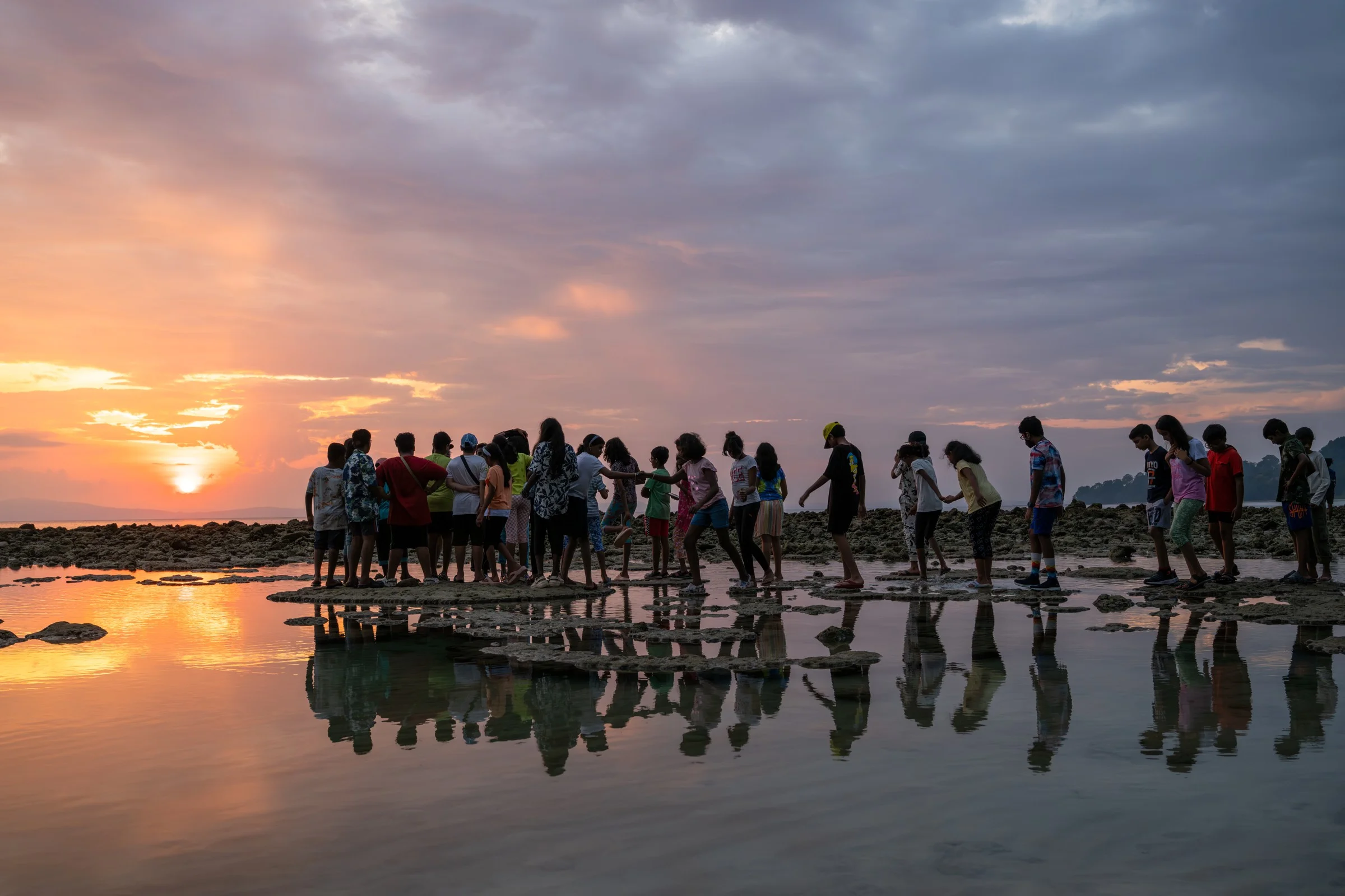 A group walking along an exposed rocky shore at sunset